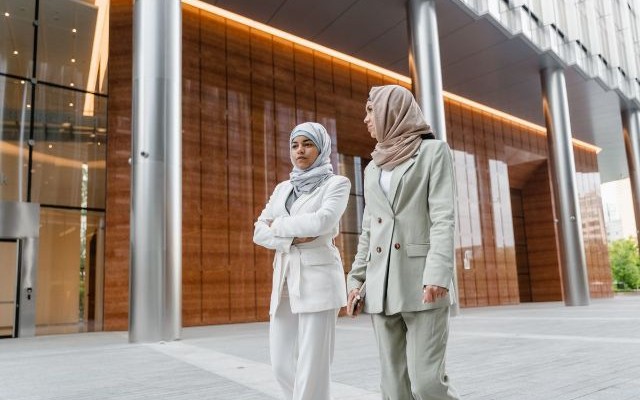 Two real estate professionals walking together outside a premium modern mixed-use development with a warm timber-and-steel facade